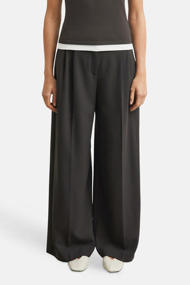 Brown wide-leg suit trousers by COMMA, featuring a smooth matte finish and front pleats, worn with a dark top and white shoes in a front view.