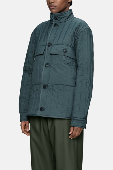 Dark green quilted women's puffer jacket with stand-up collar and front buttons, side view, worn with olive trousers