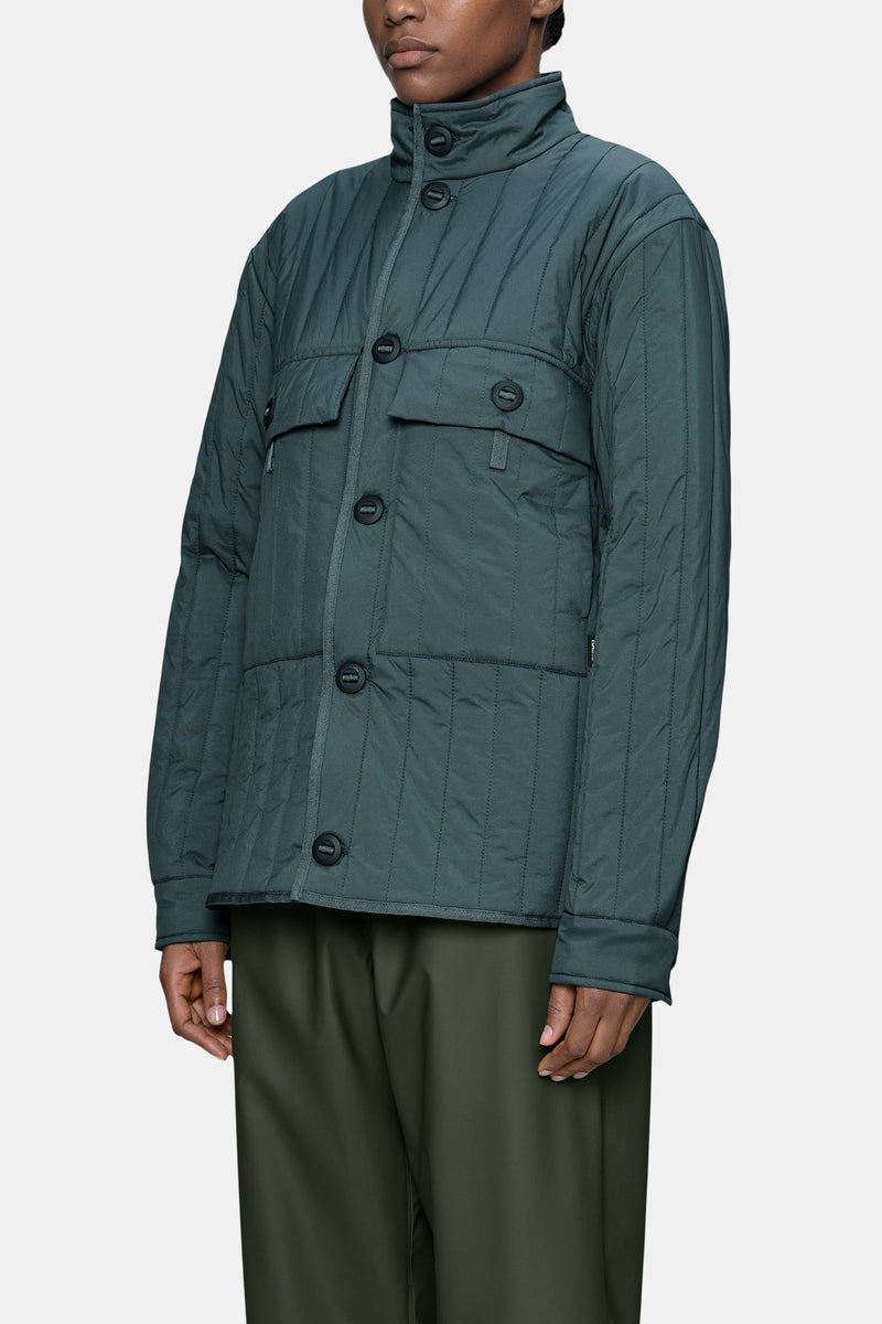 Dark green quilted women's puffer jacket with stand-up collar and front buttons, side view, worn with olive trousers