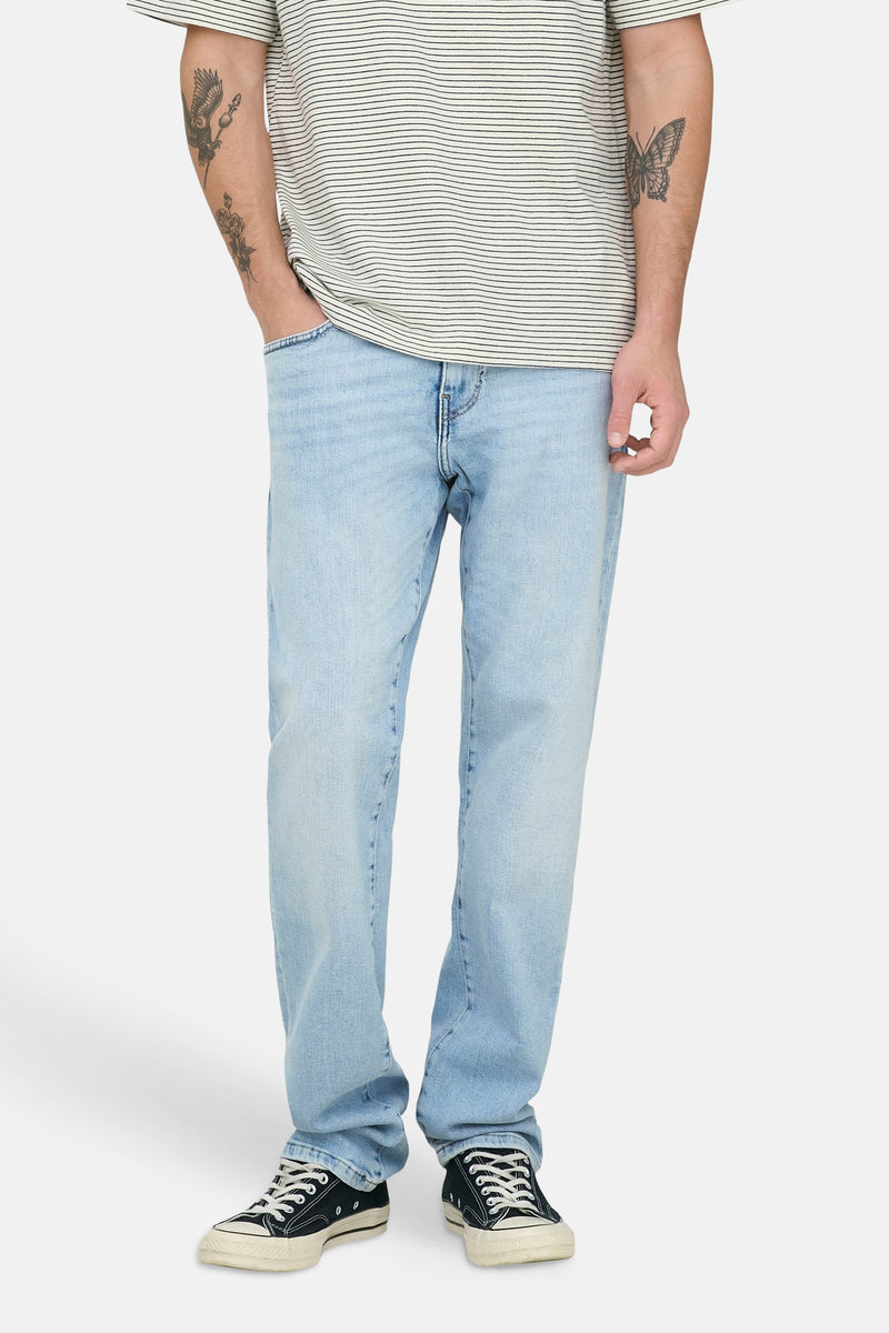 Light blue straight-leg denim jeans by WEFT, featuring faded wash and clean stitching, worn with striped tee and black sneakers, front view.