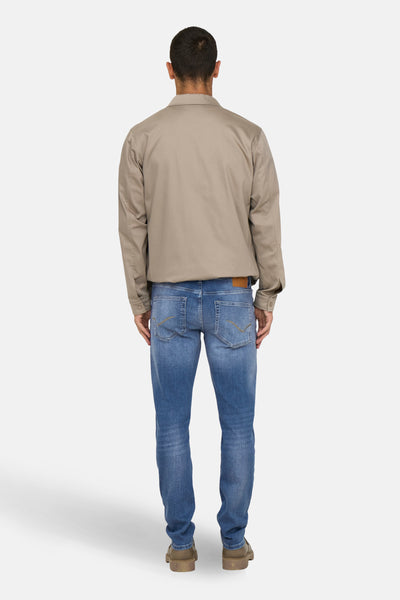 Slim jeans in medium blue denim van ONLY & SONS, met decoratieve achterzakken, gedragen met een beige jas.