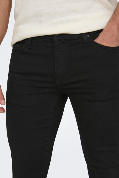 Jean slim noir de ONLY & SONS, avec une main dans la poche, porté avec un pull clair.