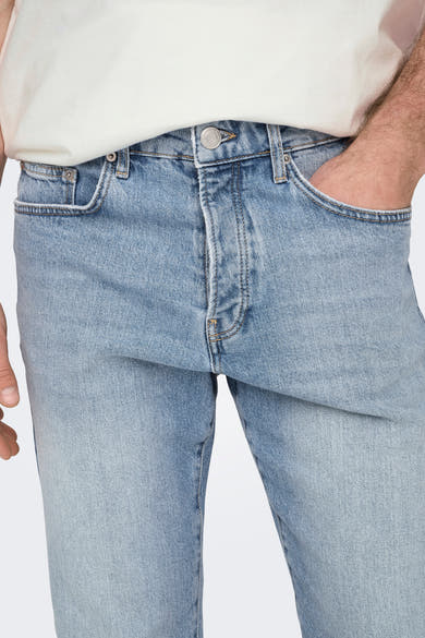 Slim-fit jeans in lichtblauw denim van ONLY & SONS®, met een hand in de zak en een wit T-shirt.