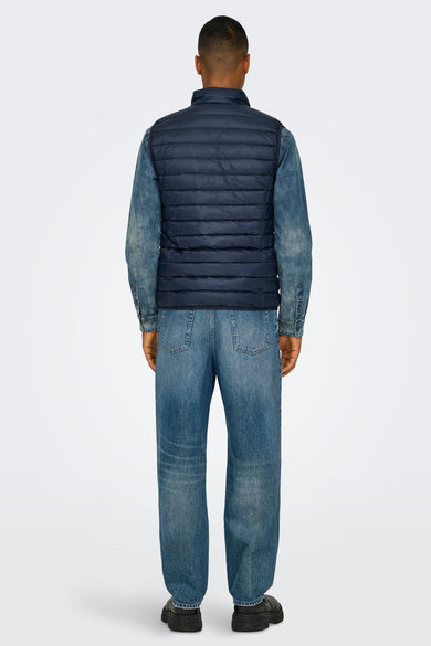 Rechte spijkerbroek in middinblauw denim van ONLY & SONS, gedragen met een spijkeroverhemd en een marineblauw gewatteerd vest.