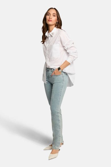 Jean droit bleu clair de Morgan de Toi, porté avec une chemise blanche à détails ornementaux.
