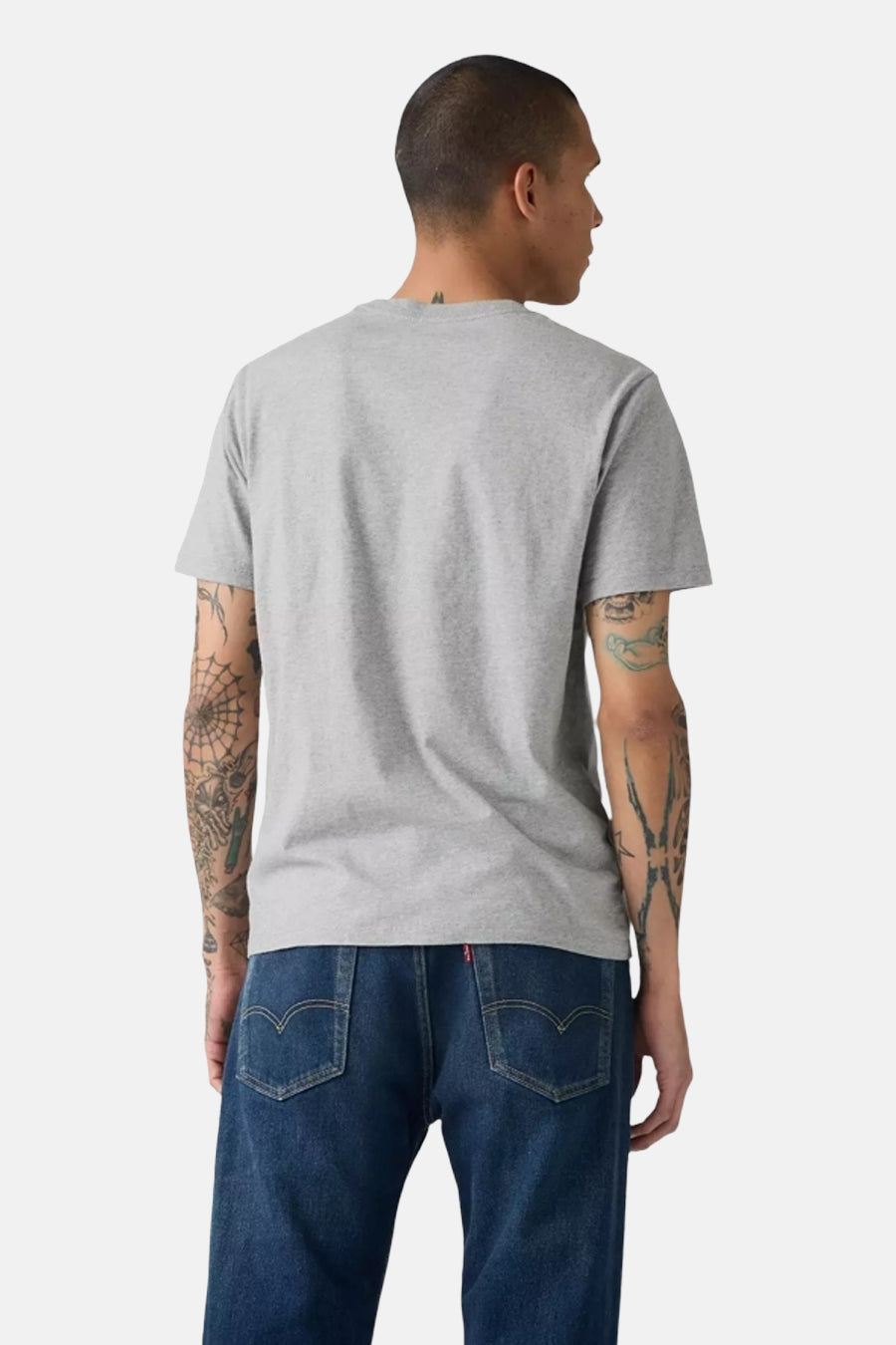 Grey short-sleeve t-shirt from back view, plain heather fabric, worn with dark blue jeans, model with tattooed arms