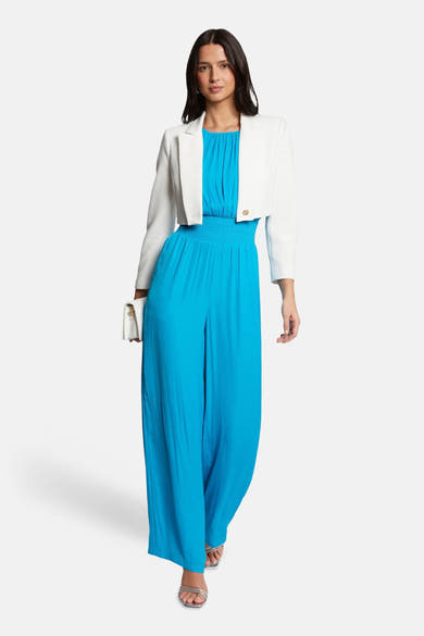 Veste écru de Morgan de Toi, portée sur une combinaison bleu turquoise et tenue avec une pochette blanche.