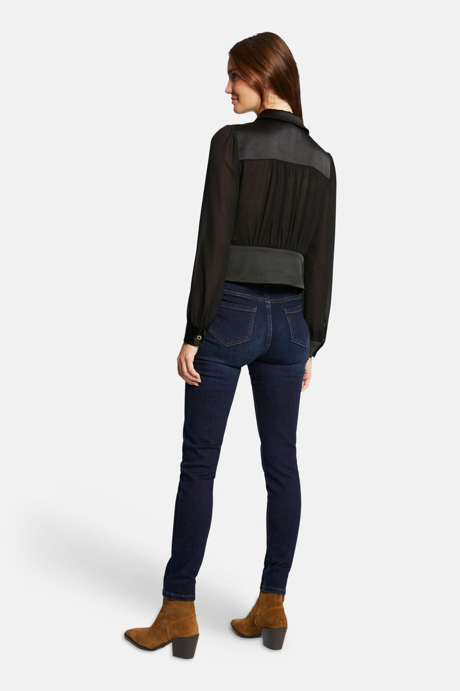 Black long-sleeve blouse with sheer fabric and gathered back, worn with dark jeans and brown boots, side view.