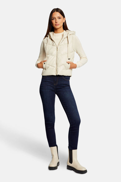 Veste sans manches écru de Morgan de Toi, avec capuche, portée sur un pull beige, un jean bleu marine et des bottines blanches.