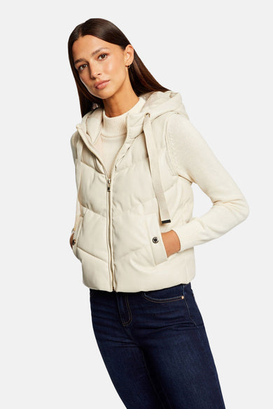 Veste sans manches écru de Morgan de Toi, matelassée, avec capuche et poches boutonnées, portée avec un pull crème et un jean bleu marine.