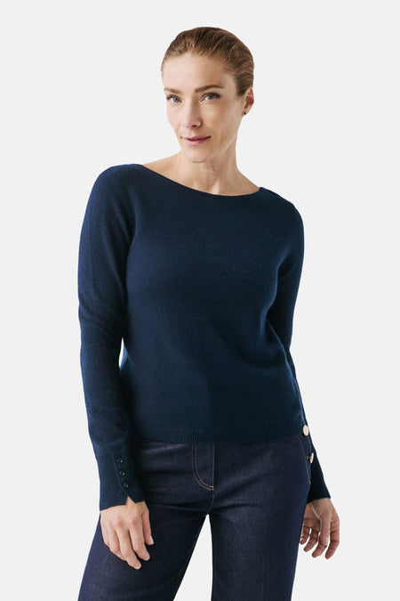 Pull à col rond bleu de CAROLL, porté avec un pantalon foncé, boutons décoratifs sur les manches et les côtés.