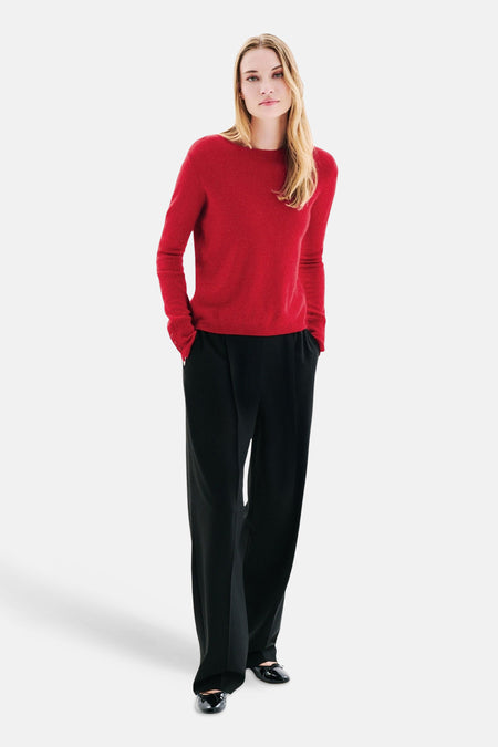 Pull à col rond rouge de CAROLL, porté avec un pantalon noir taille haute et des ballerines vernies.
