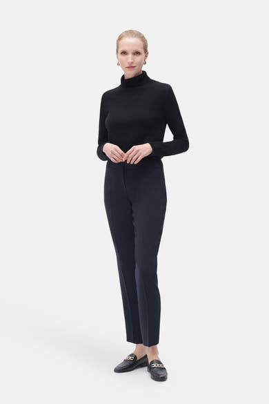 Pantalon de costume bleu de CAROLL, coupe cigarette, porté avec un pull noir et des mocassins noirs.
