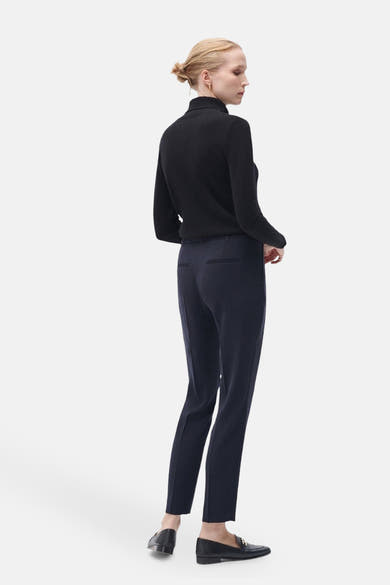 Pantalon de costume bleu marine de CAROLL, avec poches arrière passepoilées, porté avec un pull noir et des mocassins noirs.
