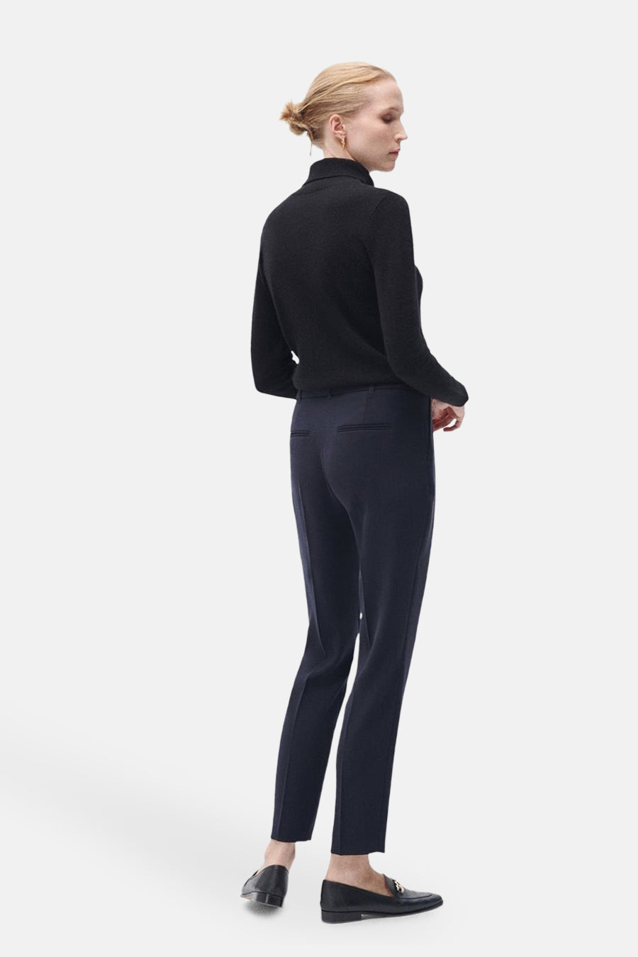 Pantalon de costume bleu marine de CAROLL, avec poches arrière passepoilées, porté avec un pull noir et des mocassins noirs.
