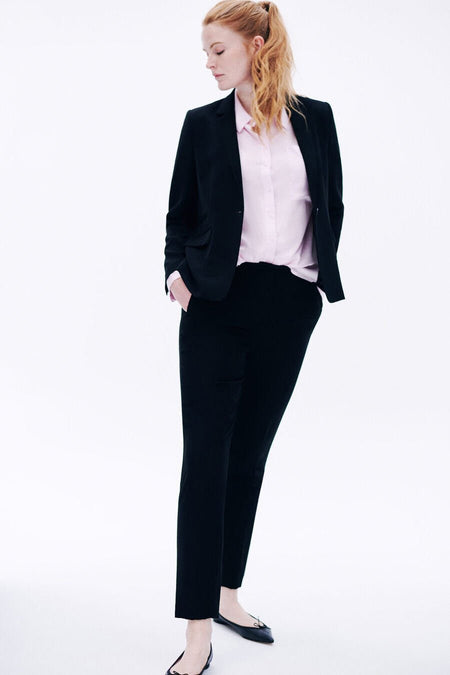 Pantalon de costume noir de CAROLL, porté avec une chemise rose et des ballerines noires.
