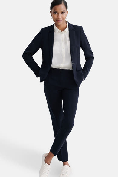 Blazer bleu marine de CAROLL, porté avec une chemise blanche et un pantalon assorti, complété par des baskets blanches.