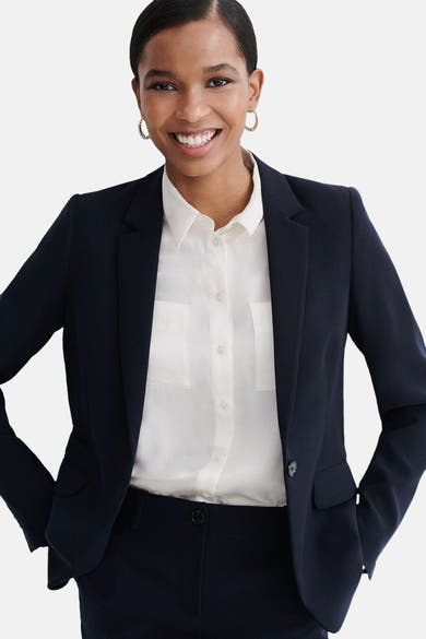 Blazer bleu de CAROLL, porté sur une chemise blanche boutonnée, avec des boucles d'oreilles dorées.