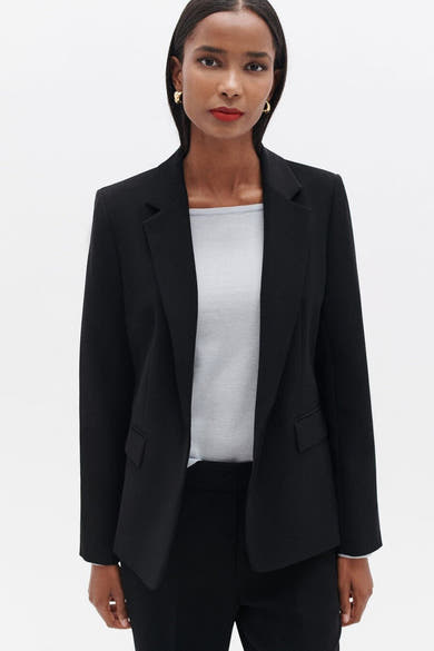 Blazer noir par CAROLL porté sur un top gris, avec des boucles d'oreilles dorées.