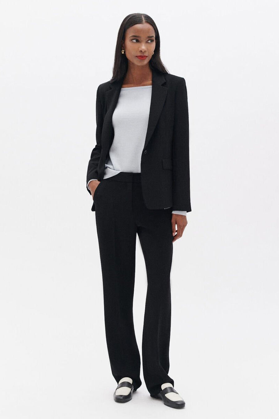 Blazer noir de CAROLL, porté avec un t-shirt gris et un pantalon noir ample, complété par des mocassins bicolores.