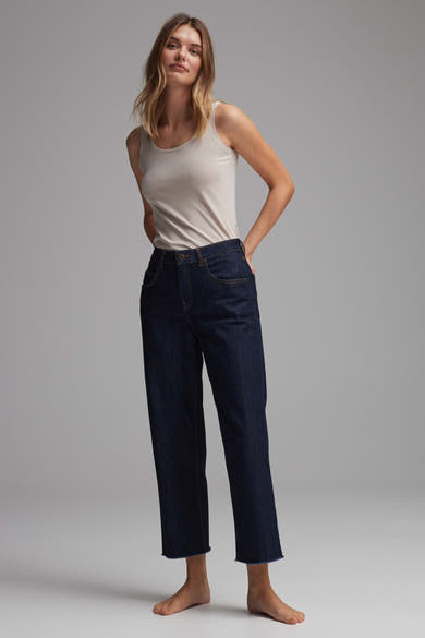 Beige tanktop van OPUS, gedragen met een donkere straight-leg jeans met rafelige zoom, voor een neutrale grijze achtergrond.