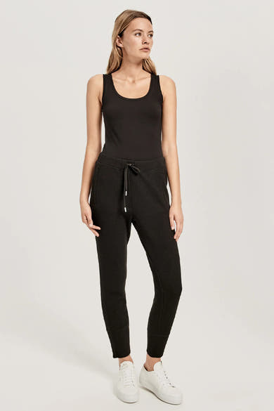 Débardeur noir de OPUS porté avec un pantalon de survêtement et des chaussures de sport blanches.