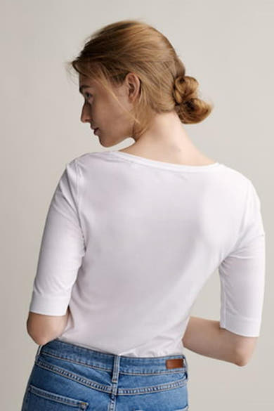 Top uni manches courtes blanc par OPUS, porté avec un jean, modèle vu de dos avec chignon.
