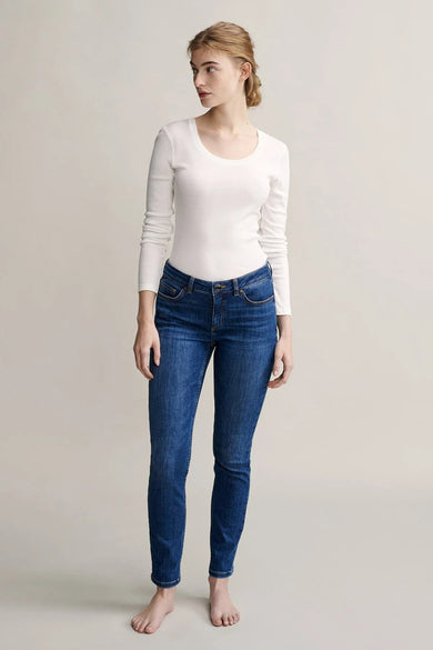 Top uni blanc à manches longues de OPUS, porté avec un jean bleu, modèle pieds nus.
