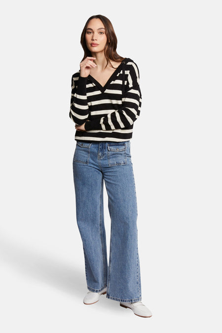 Pull à capuche multicolore de Morgan de Toi, à rayures noires et beiges, porté avec un jean bleu et des chaussures blanches.