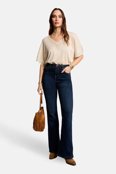 T-shirt beige à manches courtes de Morgan de Toi, avec encolure en V, porté avec un jean taille haute et un sac à franges.
