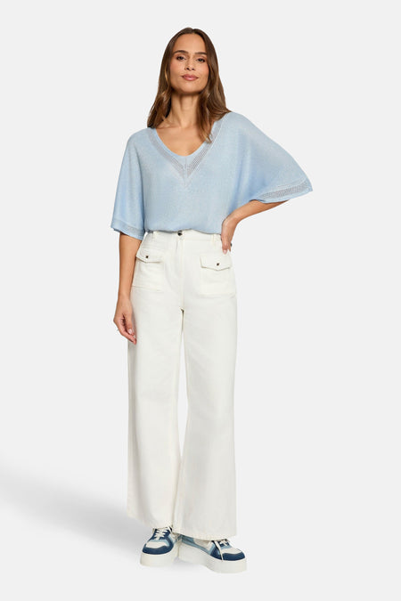 T-shirt bleu à manches courtes de Morgan de Toi, avec encolure en V ajourée, porté avec un pantalon blanc et des baskets compensées.