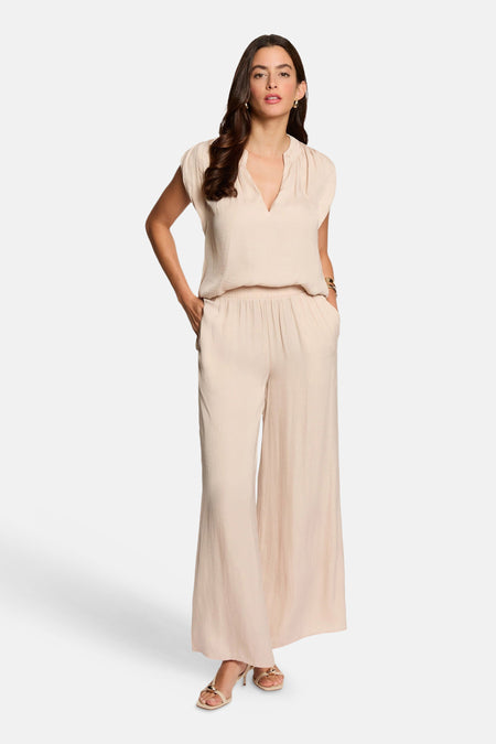 Blouse beige texturée de Morgan de Toi, sans manches, col en V, portée avec un pantalon large assorti.