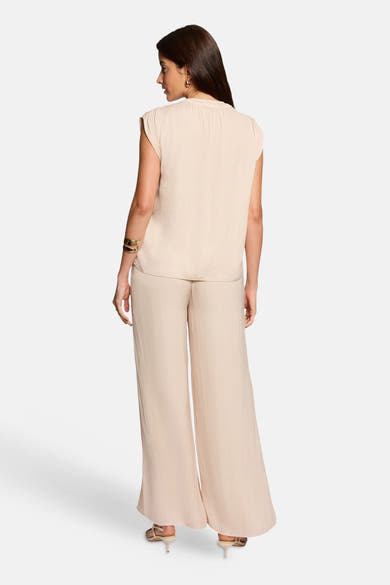 Blouse beige sans manches de Morgan de Toi, portée de dos avec un pantalon fluide assorti et des accessoires dorés.