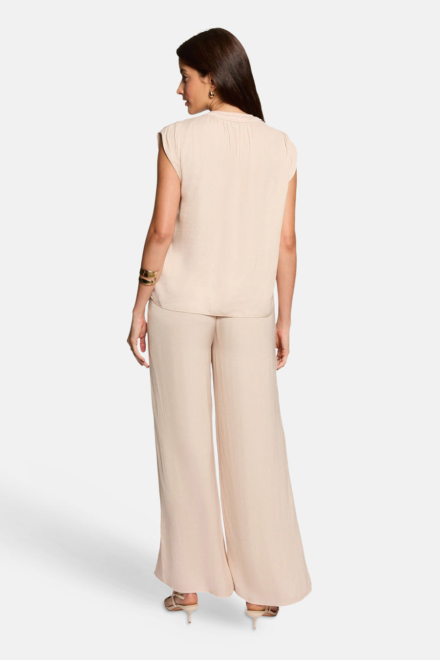 Blouse beige sans manches de Morgan de Toi, portée de dos avec un pantalon fluide assorti et des accessoires dorés.