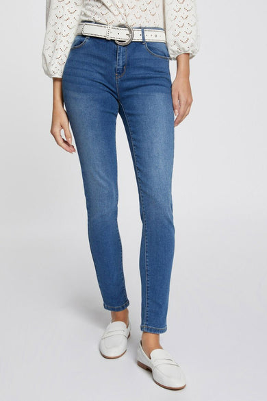 Jeans slim bleu moyen de Morgan de Toi, portés avec une ceinture blanche et des chaussures plates blanches.
