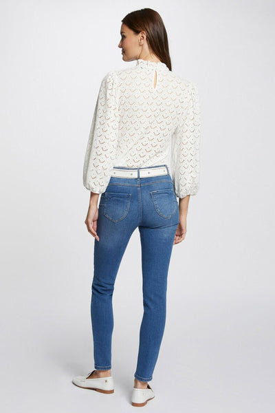 Jean slim en denim bleu moyen de Morgan de Toi, porté avec une ceinture blanche et un chemisier ajouré.
