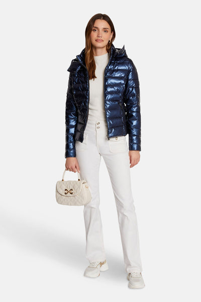 Korte, glanzende blauwe jas van Morgan de Toi, gedragen met een witte trui, een witte broek en een crèmekleurige handtas.