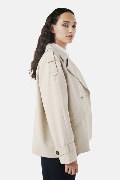 Veste courte beige de CAROLL, avec revers et poches plaquées, portée sur un haut blanc et un pantalon marine.