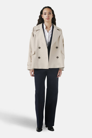 Veste courte beige de CAROLL, avec double boutonnage, portée sur un chemisier blanc et un pantalon bleu marine ample.