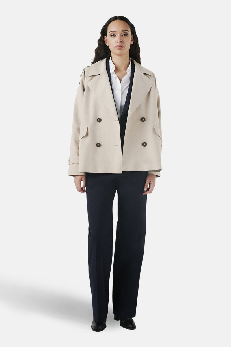 Veste courte beige de CAROLL, avec double boutonnage, portée sur un chemisier blanc et un pantalon bleu marine ample.