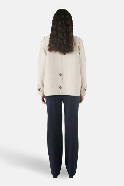 Veste courte beige de CAROLL, à boutons au dos, portée avec un pantalon large bleu marine.