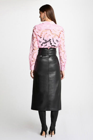 Jupe longue noire en cuir de Morgan de Toi, coupe droite, portée avec un chemisier rose ajouré et des bottines noires à talons aiguilles.