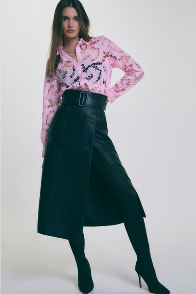 Jupe longue noire par Morgan de Toi, style portefeuille avec ceinture à boucle, portée avec des collants et un chemisier rose ajouré.