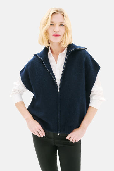 Blauwe CAROLL-gilet, zilveren ritssluiting, gedragen over een wit overhemd en een zwarte broek.