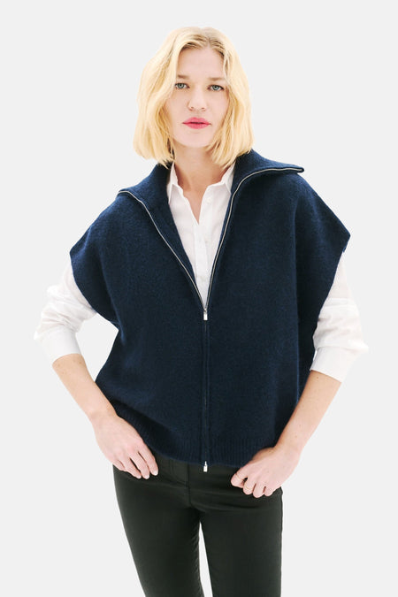 Blauwe CAROLL-gilet, zilveren ritssluiting, gedragen over een wit overhemd en een zwarte broek.