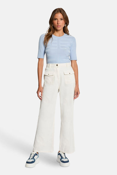 Blauwe trui met ronde hals van Morgan de Toi, gedragen met een witte broek met zakken en sleehak sneakers.