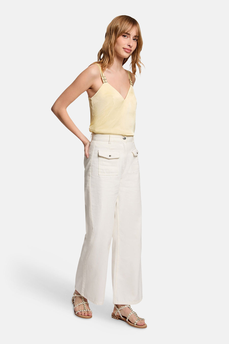 Blouse jaune sans manches de Morgan de Toi avec fines bretelles et motif texturé, portée avec un pantalon blanc et des sandales à clous.