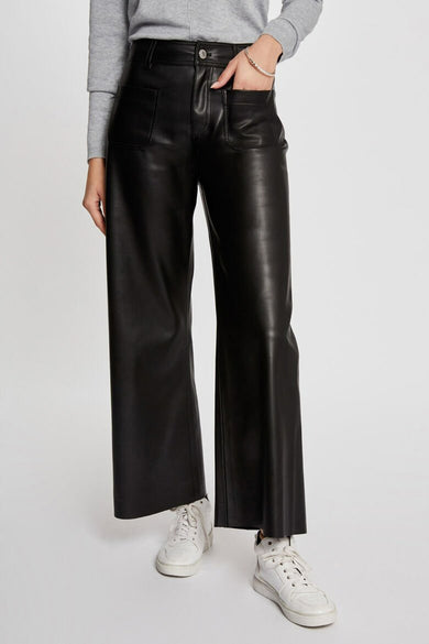 Pantalon noir en similicuir de Morgan de Toi, coupe ample, porté avec un pull gris et des baskets blanches.
