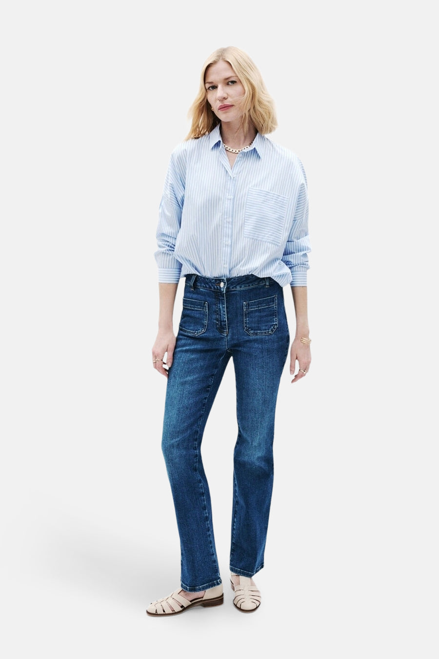 Jean bootcut bleu moyen de CAROLL, porté avec une chemise rayée et des sandales.
