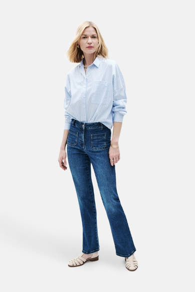 Jean bootcut bleu moyen de CAROLL, porté avec une chemise rayée bleue et blanche et des chaussures plates.
